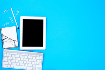 Tablet, keyboard computer with glasses and notepad on blue background