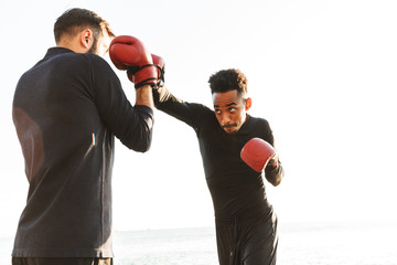 Serious handsome strong two young sports men boxers friends at the beach near sea boxing.