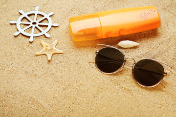 Seashells with sunglasses and cream on beach sand