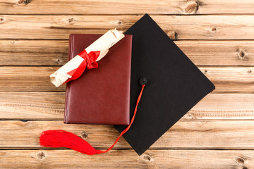 Graduation cap with diploma and book on brown wooden table