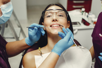 The dentist treats the girl's teeth. A young woman visited a dentist. The doctor works with an assistant