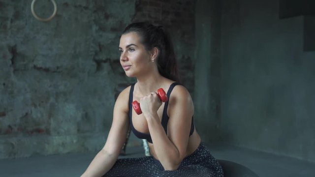 Young girl in red sportswear doing exercise with dumbbells on the background of a brick wall