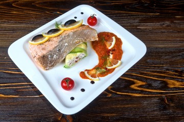 Salmon steak with lemon and stuffed Zucchini with olives and tomatoes on a white plate