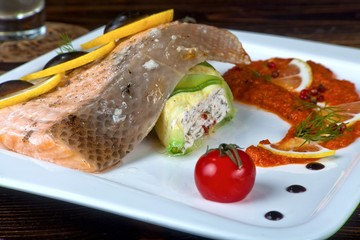 Salmon roasted with stuffed Zucchini with lemon and olives on a white plate with sauce and tomatoes