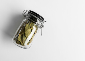 glass jar with dry bay leafs on white background