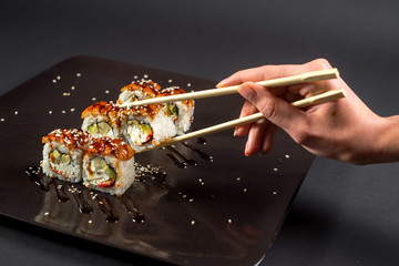 Hand with chopsticks for sushi taking a roll on dark background