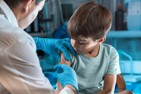 pediatrician vaccinating little boy in the pediatric clinic / doctor holding syringe subcutaneous vaccine for child in the medical office 