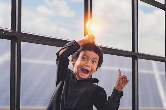 Child With Future Of Alternative Energy And Sustainable Energy. Funny Asian Boys Hold A Light Bulb That Shines In Their Hands At Solar Panel, Photovoltaic. Eco-Friendly And Pure Energy Concept