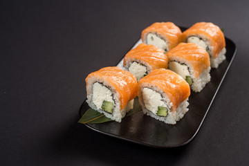Close up sushi rolls in a black plate on dark background