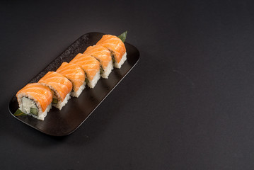 Close up sushi rolls in a black plate on dark background