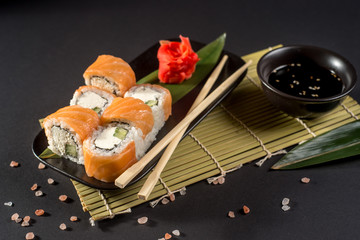 Close up sushi rolls in a black plate on dark background