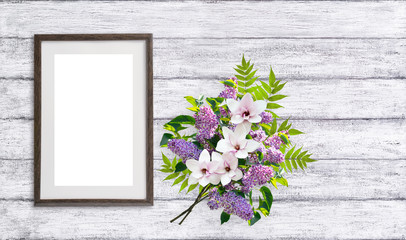 Floral bouquet with lilacs, magnolia flowers and empty motivationall picture frame on shabby wooden background. Copy space for photo or text.