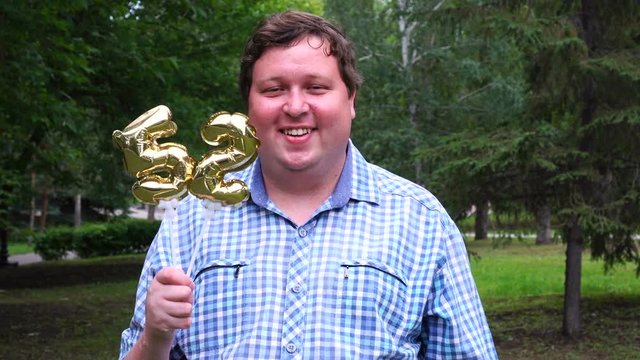Big man holding golden balloons making the 52 number outdoor. 52th anniversary celebration party