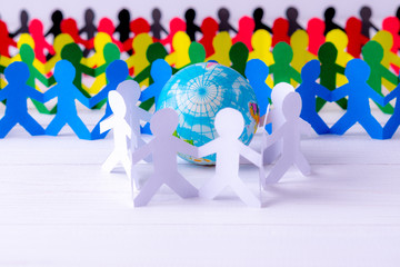 Circle of paper people holding hands around the globe made of paper cut . World Population Day.