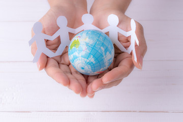 Closeup woman hands holding globe with white people chain made from paper cut. World population day.