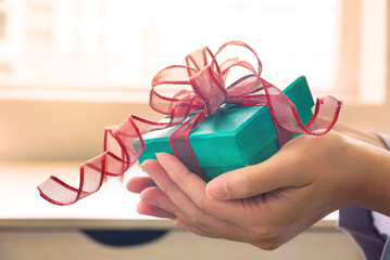 Woman give green gift box with background warm light from window.