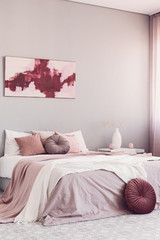 Round beige pillow on white bed in classy bedroom interior with abstract painting on the wall