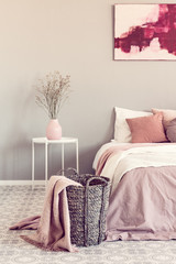 Pastel pink blanket on wicker basket in stylish bedroom interior