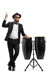 Male musician in a suit posing next to conga drums and pointing up