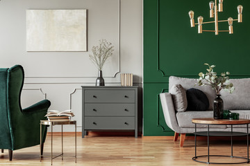 Fashionable living room interior with wooden commode, scandinavian sofa and emerald green armchair