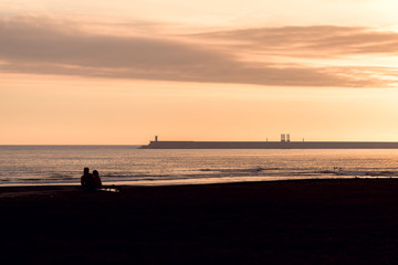 Two people watching the beautiful sunset by the sea and the cruise terminal, Matosinhos, Portugal. Beautiful sunset at Matosinhos beach in Porto, Portugal.