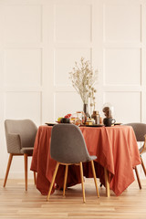Dry flowers in vase on dining table covered with dark orange tablecloth