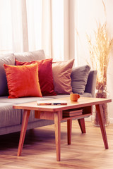 Orange, red and beige pillows on grey comfortable couch in chic living room interior