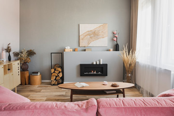 Stylish living room interior with pastel pink sofa, wooden coffee table and eco fireplace