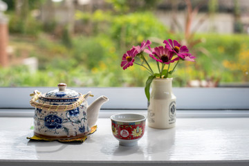 Tea time, Chinese teapot and cup Near the flower vase, Outside is garden view.