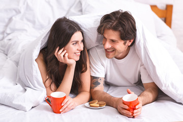 Obraz na płótnie Canvas Young couple having breakfast in bed, hiding under blanket