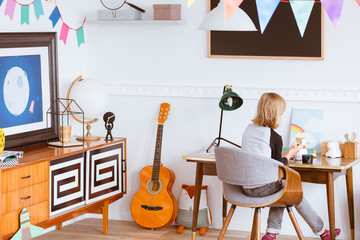 Kid sitting at the wooden desk in her artistic vintage styled bedroom