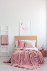 Pastel pink pillow and blanket on single wooden bed with white bedding in scandinavian bedroom...