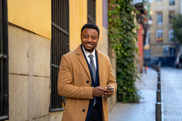 Young handsome businessman using mobile phone app sending message outside office in urban city