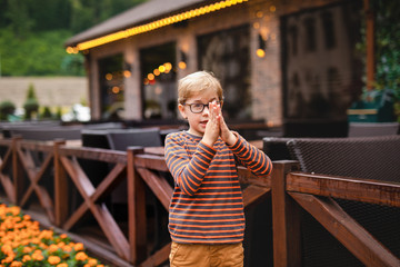 Strong, smart and funny little boy playing outdoors, wearing eyeglasses. Problem with eyes, astigmatism