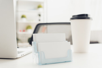 card holder with empty business cards near paper cup and laptop on office desk