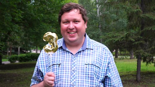 Big man holding golden balloon making the 3 number outdoor. 3th anniversary celebration party