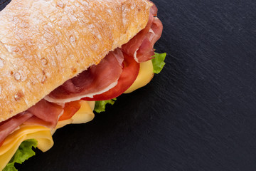 Ciabatta sandwich with lettuce , prosciutto and  cheese over stone background. Top view with copy...