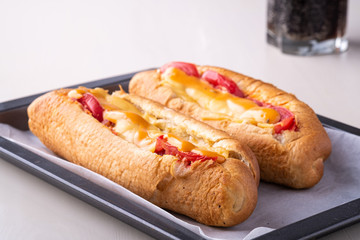 Two hot dog fast food junk fresh sausage cheese sauce isolated on baking tray with single glass of cola drink white background