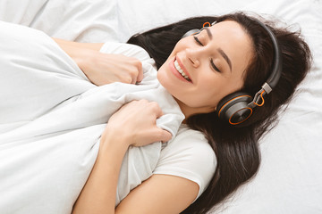 Happy young woman enjoying music in bed