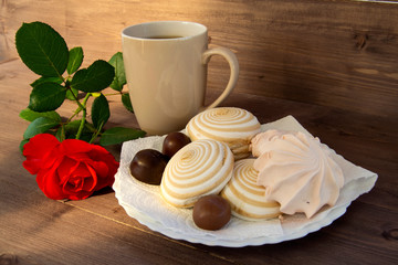 Delicate multicolored marshmallows on white openwork plate. Still life with marshmallows, a Cup of tea and a rose on vintage background.