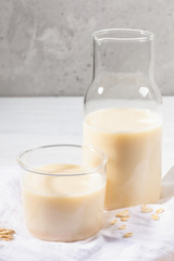Close-up glass of dairy free oat milk and flakes on white napkin on concrete background.