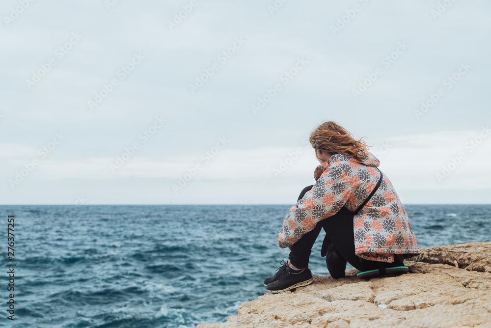 Wall mural woman sitting on the cliff with sad view looking at storming sea