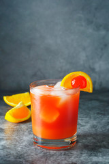 Summer cocktail. Orange juice with mint, syrop, fruit slices and cherry with ice. Dark background.