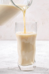 Close-up oat milk is pouring from glass decanter into figured glass.