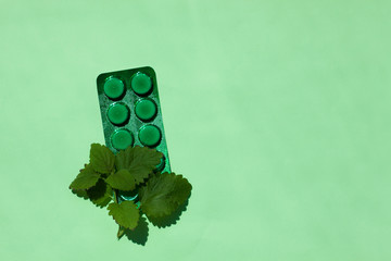 A green medical tablets plate with mint leaves, a remedy against allergy and runny nose, colds,...
