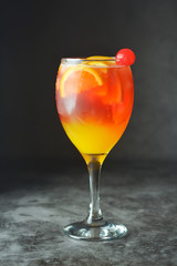 Summer cocktail. Orange juice with mint, syrop, fruit slices and cherry with ice. Dark background.