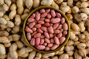 Bronze bowl of peeled peanuts and peanuts in nutshell