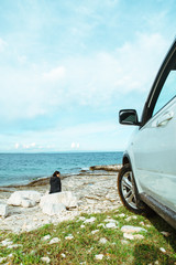 Fototapeta na wymiar woman sitting at rock near suv car at seaside enjoying the view