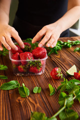 woman picks strawberries. berries in a plastic container. lime, strawberry, mint - ingredients for making lemonade on brown wooden table