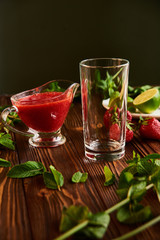 empty glass for smoothies. lime, strawberry, mint - ingredients for making lemonade on brown wooden table